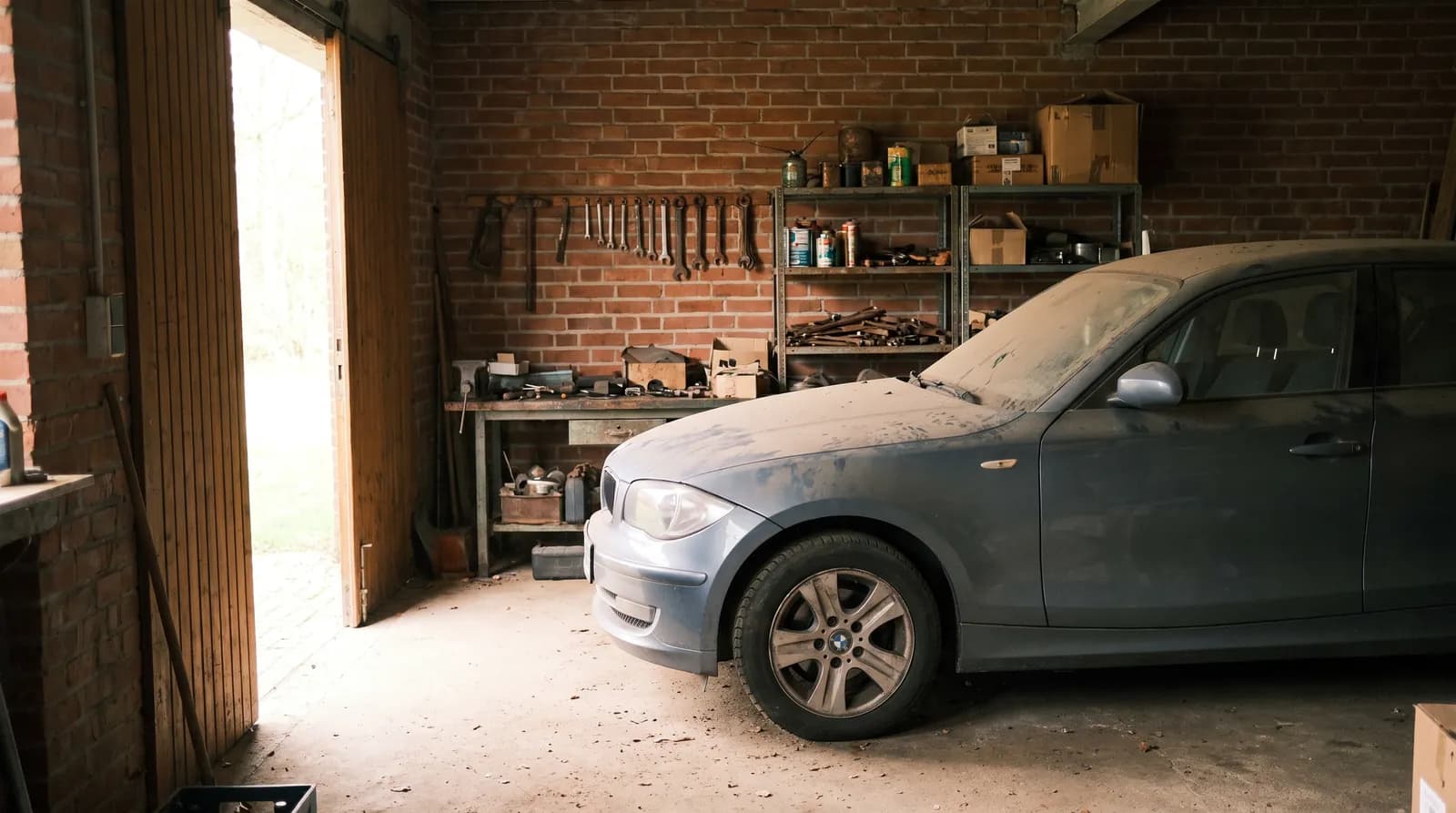 Verstaubter Kleinwagen steht in einer Backsteingarage mit halb geöffnetem Tor